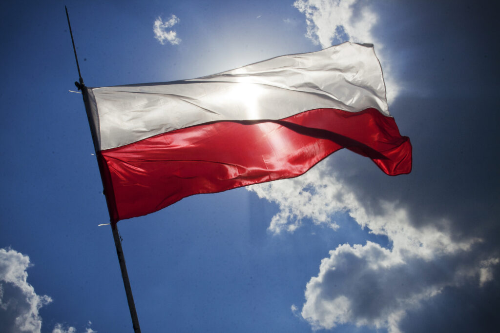 Polska flaga na maszcie w tle niebo z chmurami