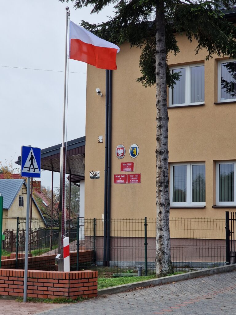 zdjęcie przedstawia budynek urzędu i masz z biało-czerwoną flagą przed nim
