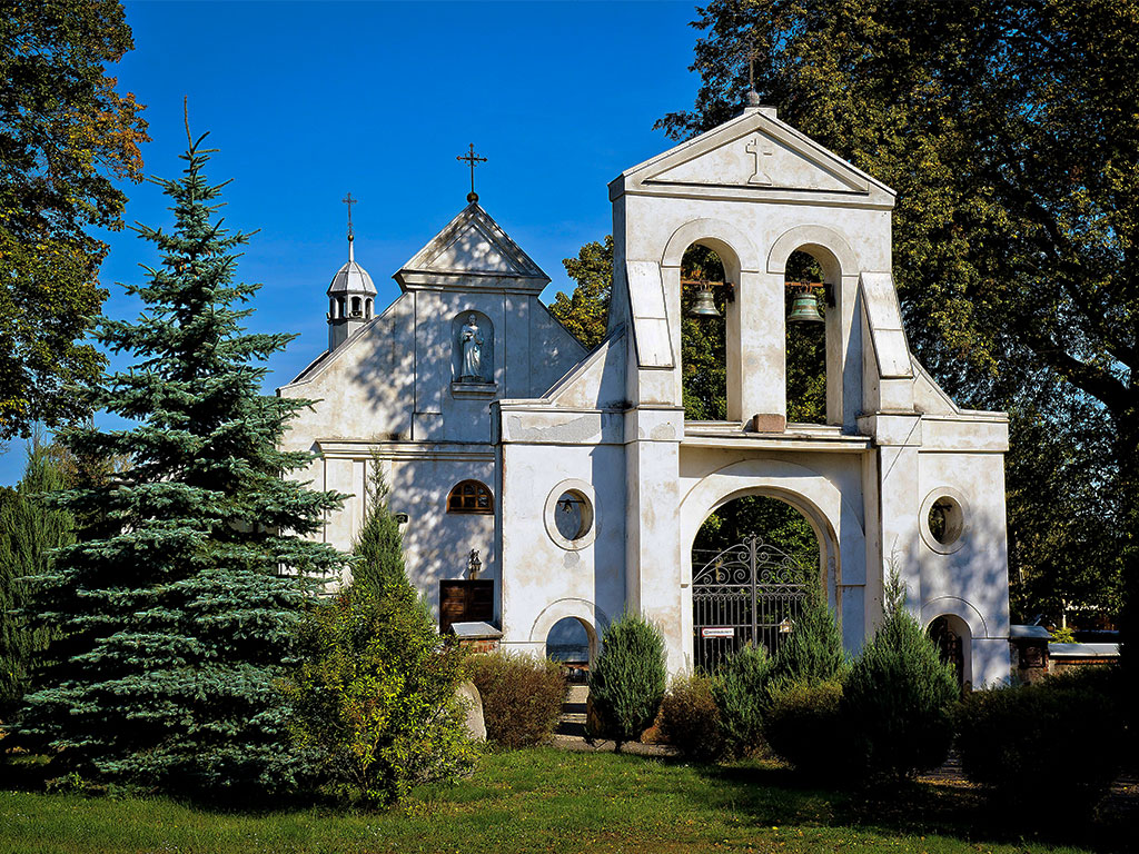 Brama i kościół w otoczeniu zieleni drzew w tle niebieskie niebo