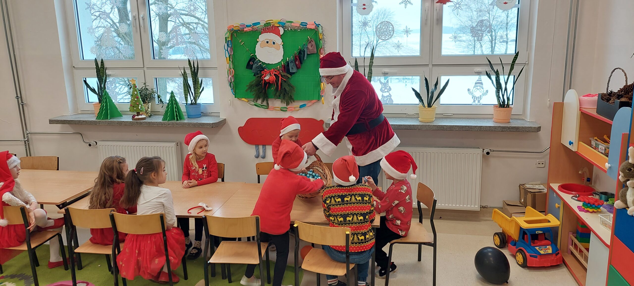 dzieci siedzą w ławkach obok nich wójt przebrany w strój mikołaja rozdający cukierki