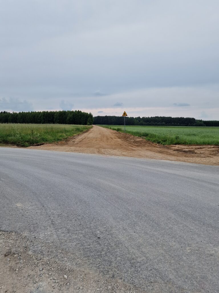 Na obrazie widocznym nieutwardzonej drogi, która przepływa przez środek otwartego pola. Po obu drogach podróży są zielone i nieregularne tereny, które zawierają inne struktury czy drogi.