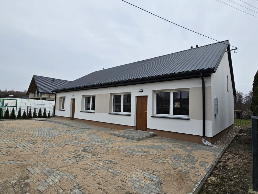 Na obrazku widocznym jest dom z białym dachem oraz czarnym, metalowym dachem. Obie konstrukcje, różne rodzaje materiałów, są elementami tej samej konstrukcji.