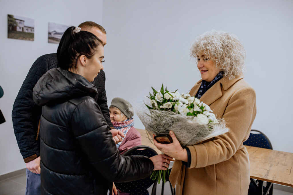 Na obrazku kobiety, który przekazuje bukiet kwiatów grupy ludzi. Każda dama z kwiatami, jak i osoba odbierająca prezent, mogą być zadowolone i radosne.