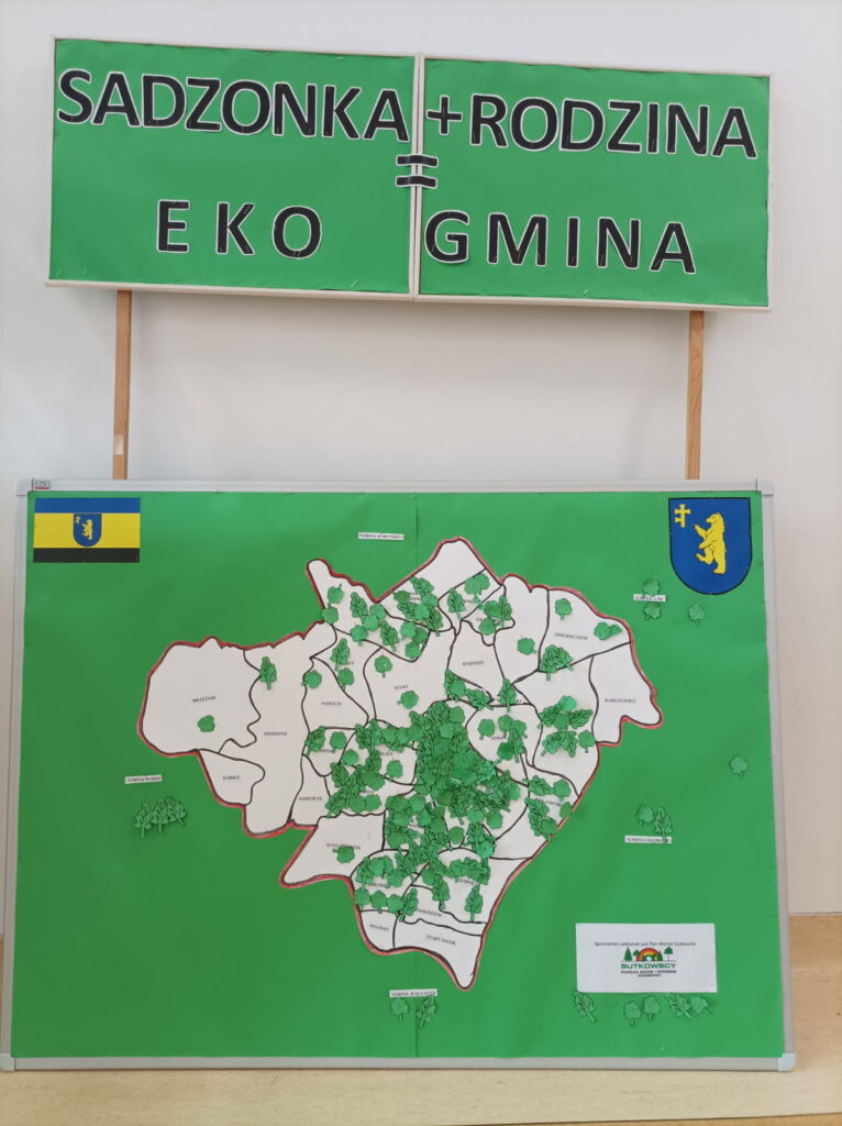 Zielony plakat z napisem „Sadzonka + Rodzina = Eko Gmina”. Na dole mapa z drzewami. Widoczny jest herb gminy.