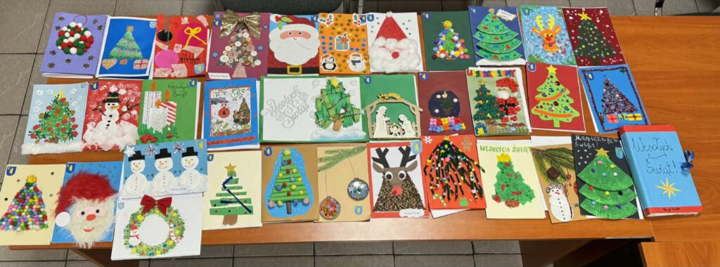 Zdjęcie przedstawia ręcznie robione kartki świąteczne na drewnianym stole. Kartki są kolorowe, z motywami choinek i Świętego Mikołaja. Tło jest jasne i neutralne.