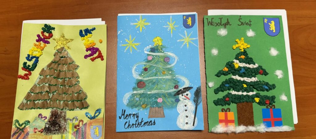 Trzy ręcznie robione kartki świąteczne z choinkami. Kolory: zielony, niebieski, brązowy, białe detale. Tło brązowe.