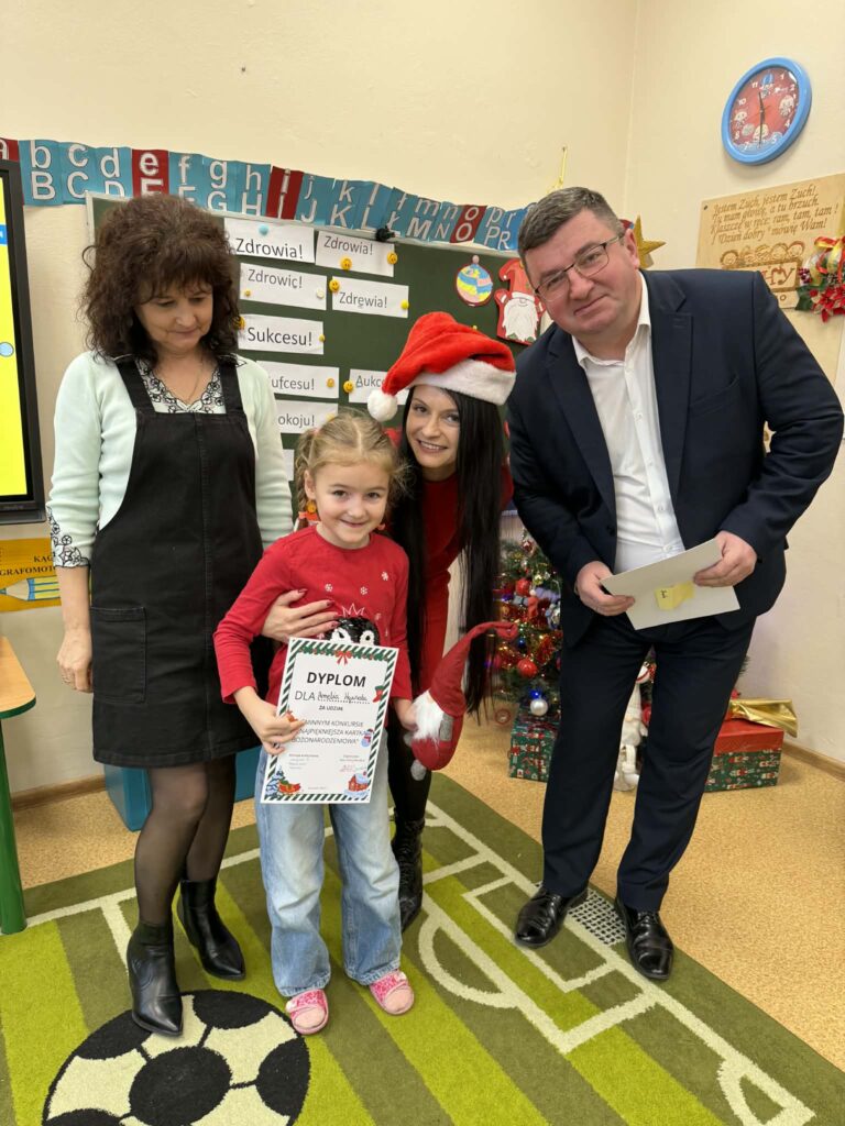 Na zdjęciu są cztery osoby: dziecko z dyplomem, dwie kobiety i mężczyzna. Kobieta pośrodku ma czerwoną czapkę Mikołaja. Tło stanowią zielone tablice z alfabetem i świąteczna dekoracja.