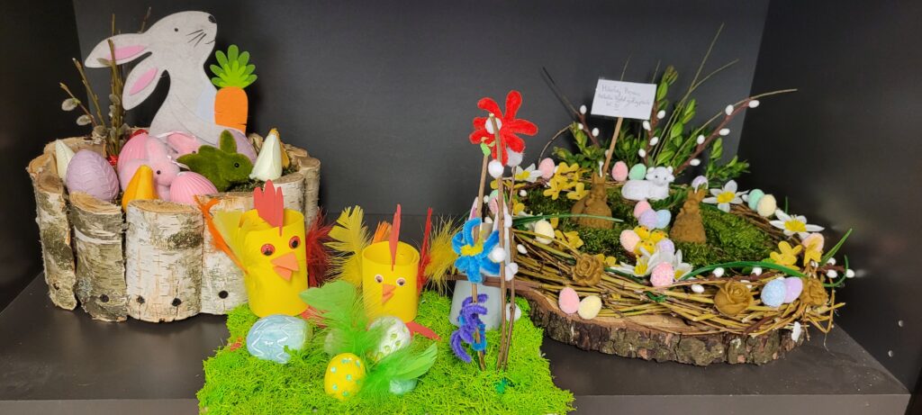 Dekoracje wielkanocne na czarnym tle: koszyczki z pisankami, filcowe zające i kurczaki, kolorowe kwiaty z materiału.