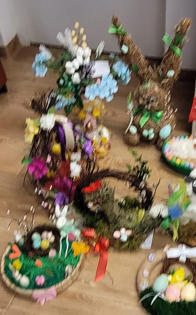 Kolorowe, świąteczne ozdoby na jasnym tle. Kompozycje z kwiatami, zającem i jajkami wielkanocnymi. Dominują zieleń i pastele.