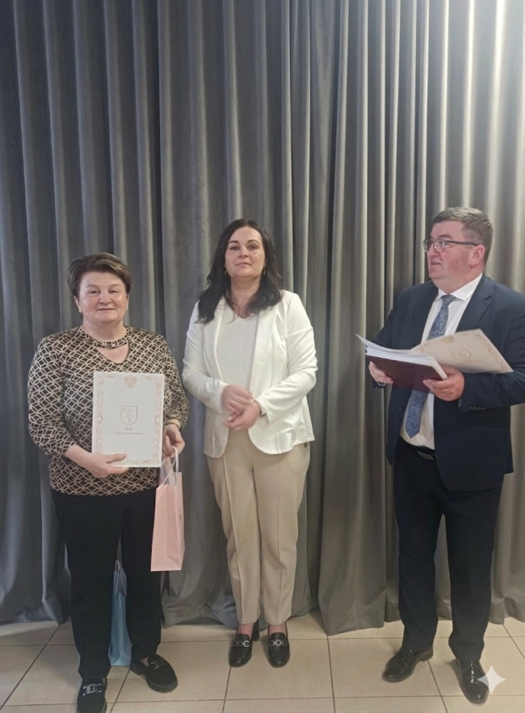 Trzy osoby pozują przed szarymi zasłonami. Kobieta po lewej trzyma dokument. Mężczyzna po prawej ma granatowy garnitur.